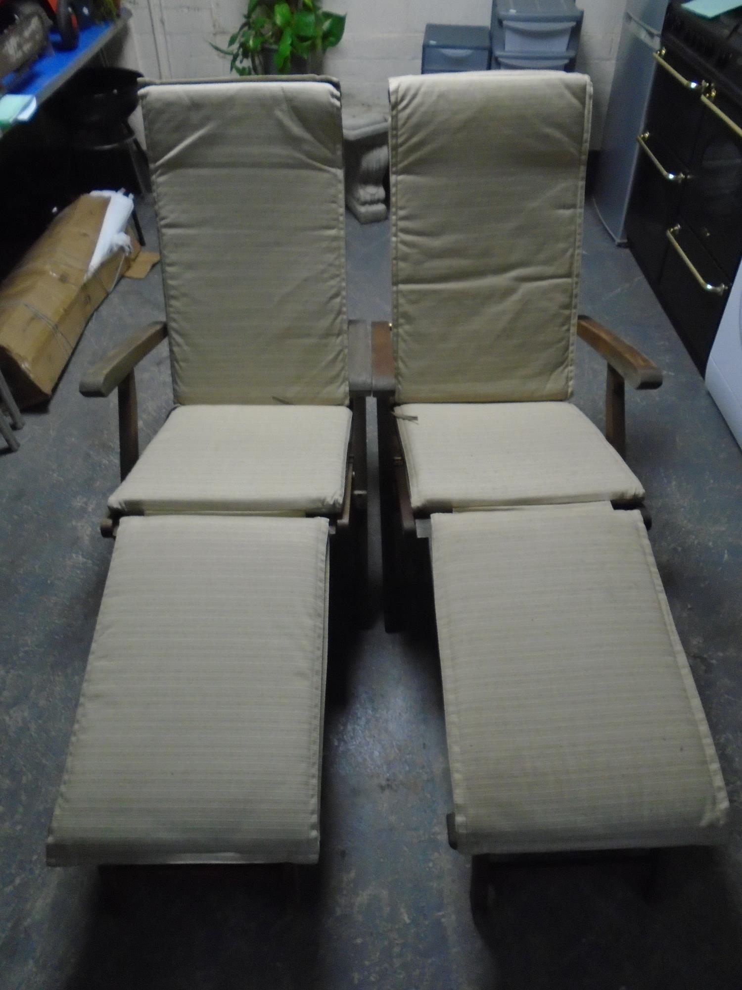 A pair teak steamer garden armchairs with footrests and cushions.