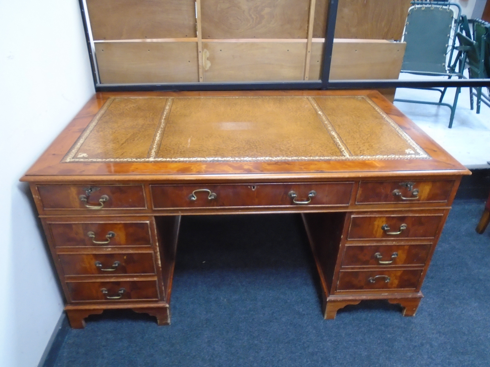 A yew wood nine drawer twin pedestal writing desk with a brown tooled leather inset panel,