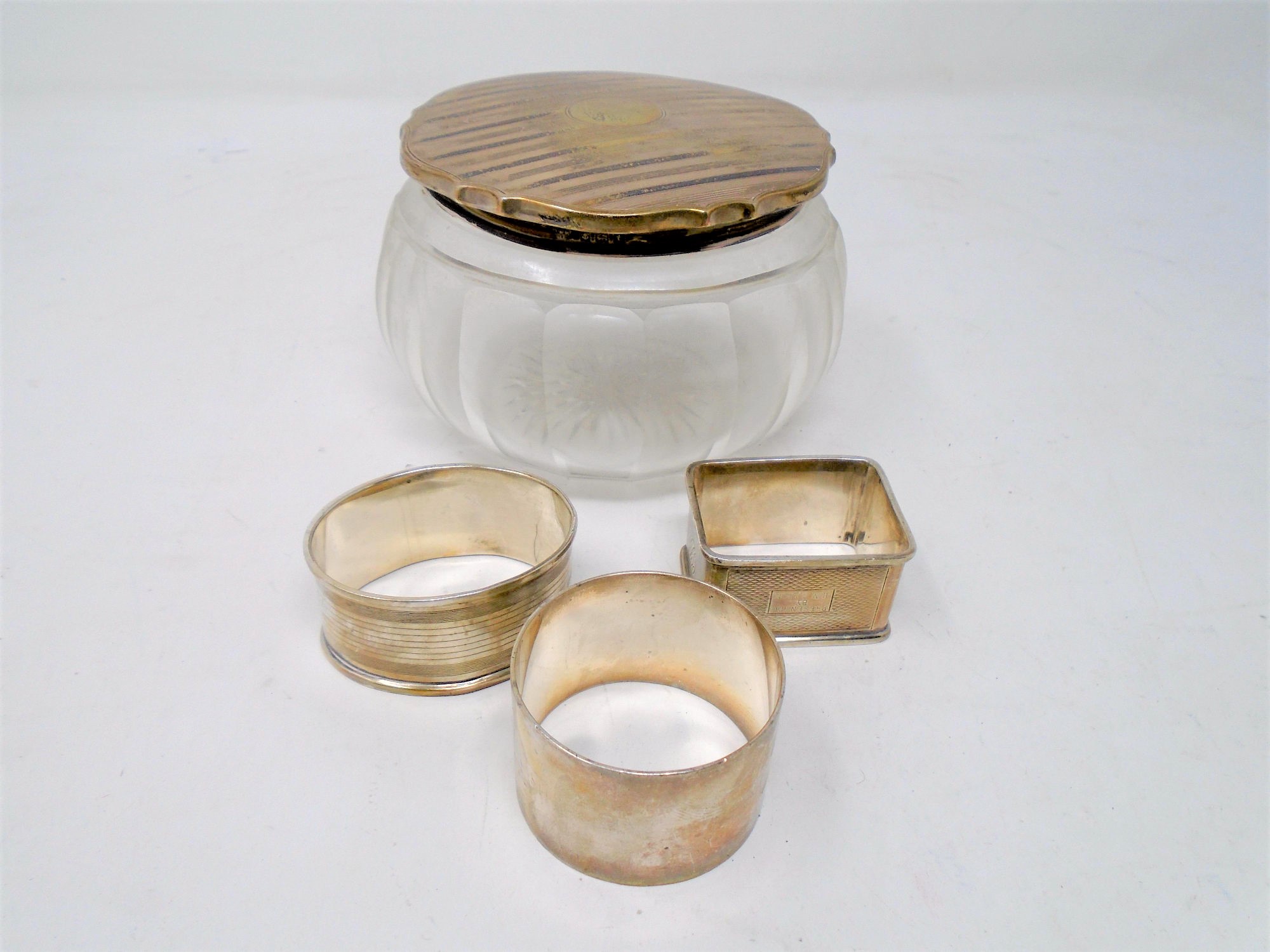 Three silver napkin rings together with a silver lidded glass dressing table jar.