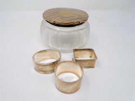 Three silver napkin rings together with a silver lidded glass dressing table jar.