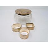 Three silver napkin rings together with a silver lidded glass dressing table jar.