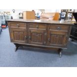 A triple door oak linen fold sideboard on raised legs fitted with drawers above.