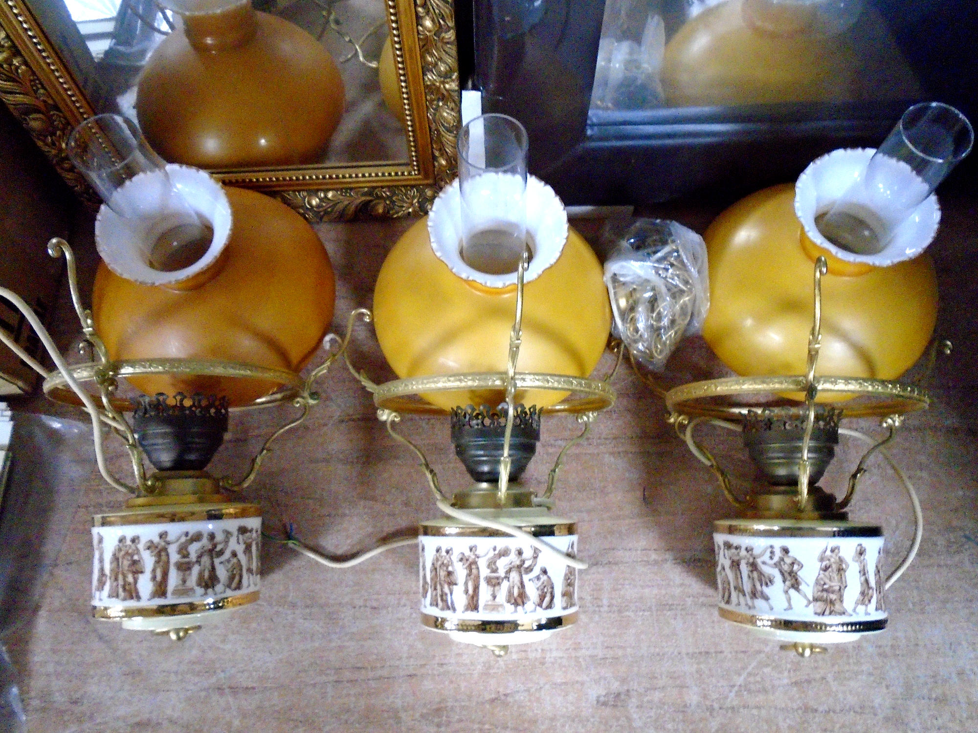 Three ceramic hanging oil lamps with amber shades and chimneys depicting Grecian figures.
