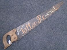 An antique woodworking saw with tattoo removal advertising.