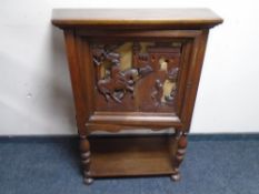 A Continental oak cabinet with carved panel door on raised legs with undershelf.