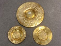 A brass Arts and Crafts charger, diameter 43 cm, together with two further smaller plaques.