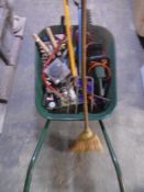 A metal wheelbarrow containing assorted garden tools including electric hedge trimmer.