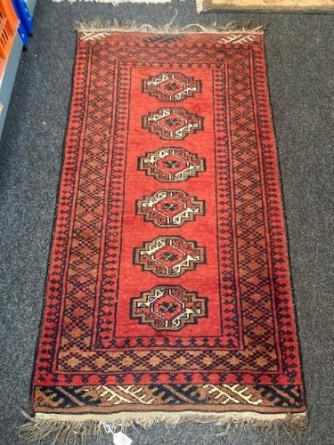 An Afghan fringed rug on red ground.