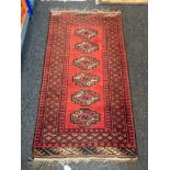 An Afghan fringed rug on red ground.