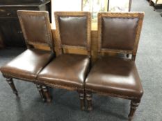 A set of six carved Edwardian oak dining chairs upholstered in brown studded leather.