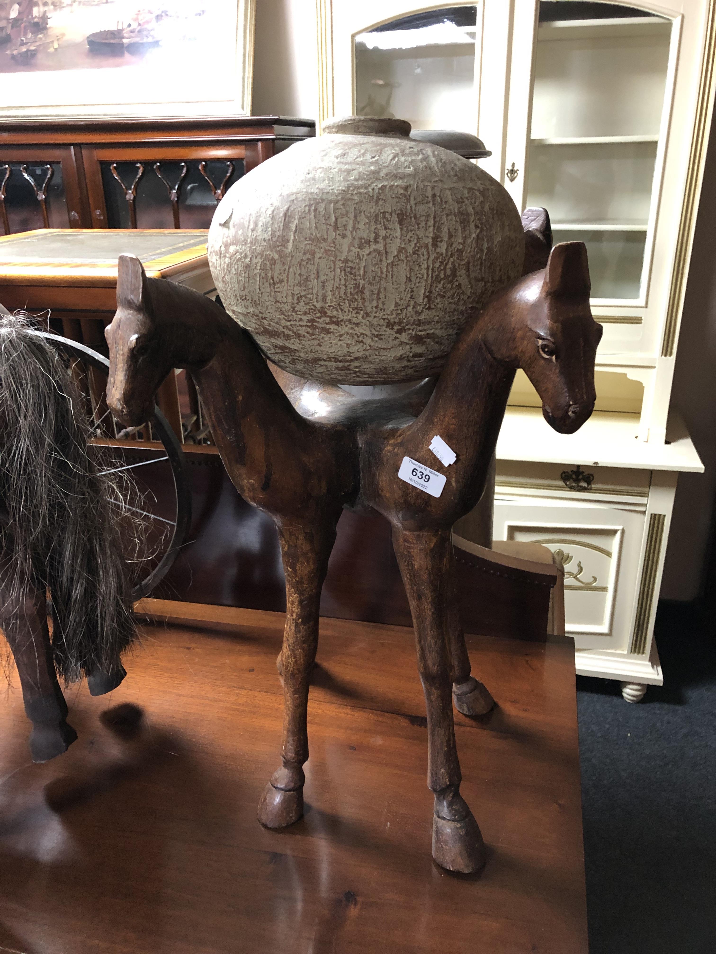 A globular pottery vase on a carved hardwood horse head four-way stand.