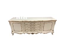 A cream and gilt shaped fronted double door buffet sideboard fitted with four central drawers width