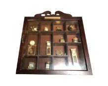 A display case containing a quantity of miniature brass timepieces.
