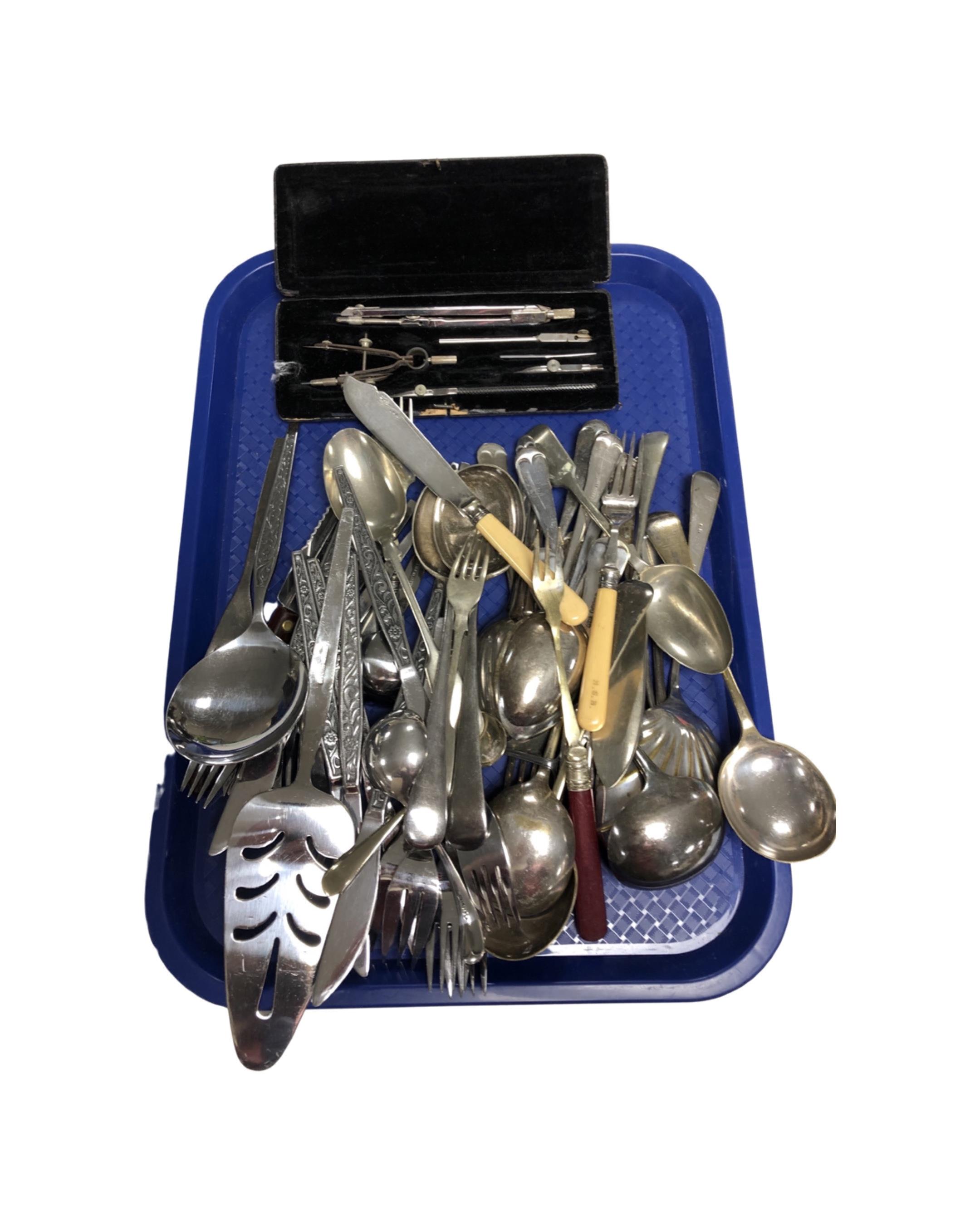 A tray containing a cased drawing set, assorted plated and stainless steel cutlery.