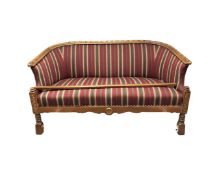 A 20th century carved oak framed curved backed settee in striped fabric (lower stretcher detached)