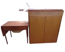 A mid-20th century teak flap sided sewing table together with a double door cabinet and a wall