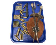 A tray of spent ammunition casings, a plaque with two swords, a cannon desk ornament,