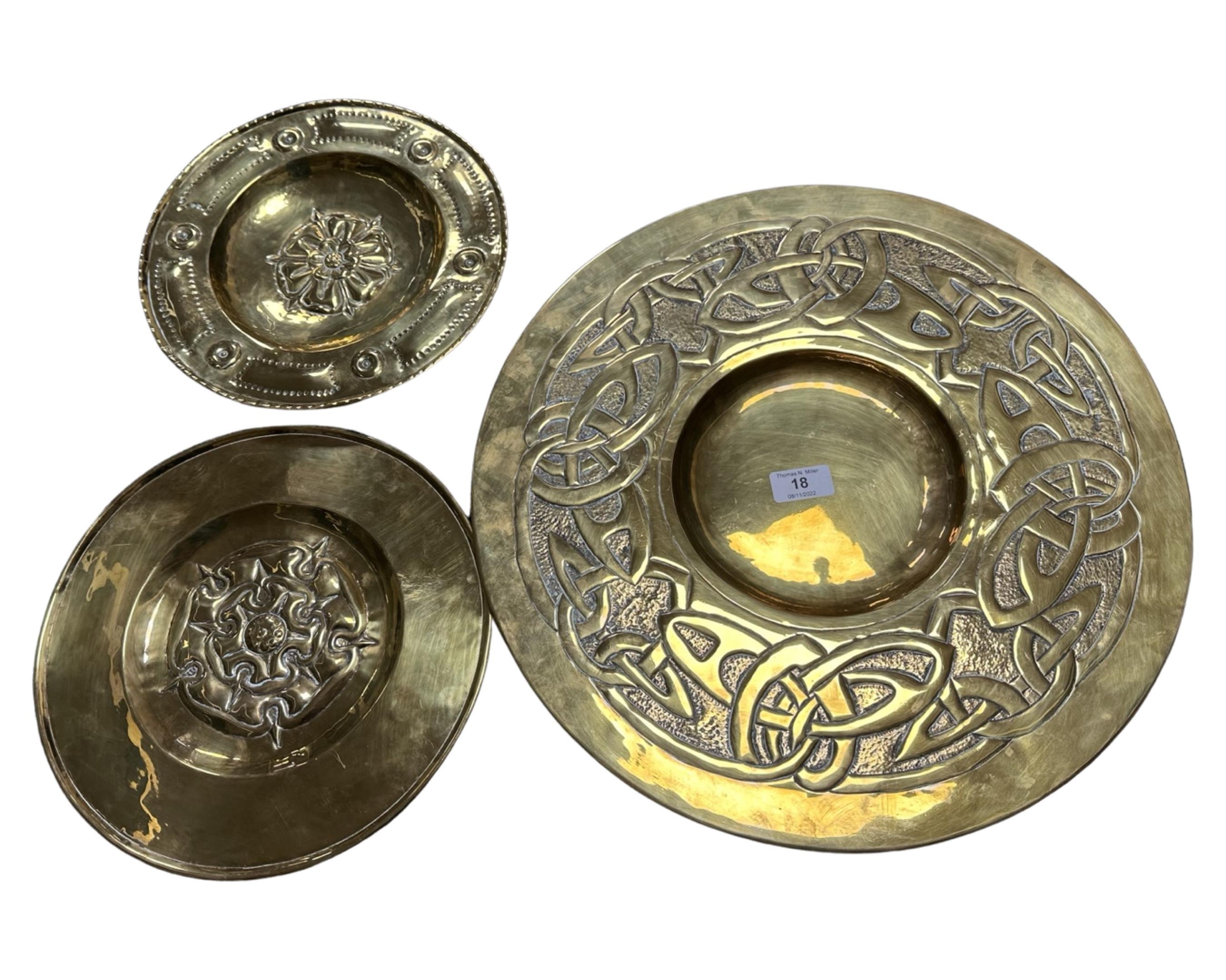 A brass Arts and Crafts charger, diameter 43 cm, together with two further smaller plaques.