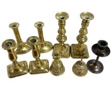 A tray containing three pairs of brass candlesticks, a further candlestick and two brass hand bells.