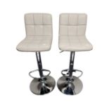 A pair of contemporary chrome gas lift barstools upholstered in cream vinyl.