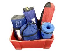 A crate containing camping equipment including tents, sleeping bags, sleeping mat roll.