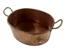 A vintage oval copper pan with brass handles.