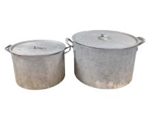 Two large graduated aluminium cooking pots with lids.