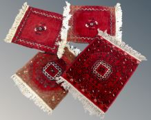 Four small Afghan fringed rugs on red ground.