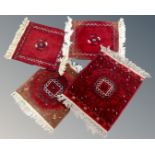 Four small Afghan fringed rugs on red ground.