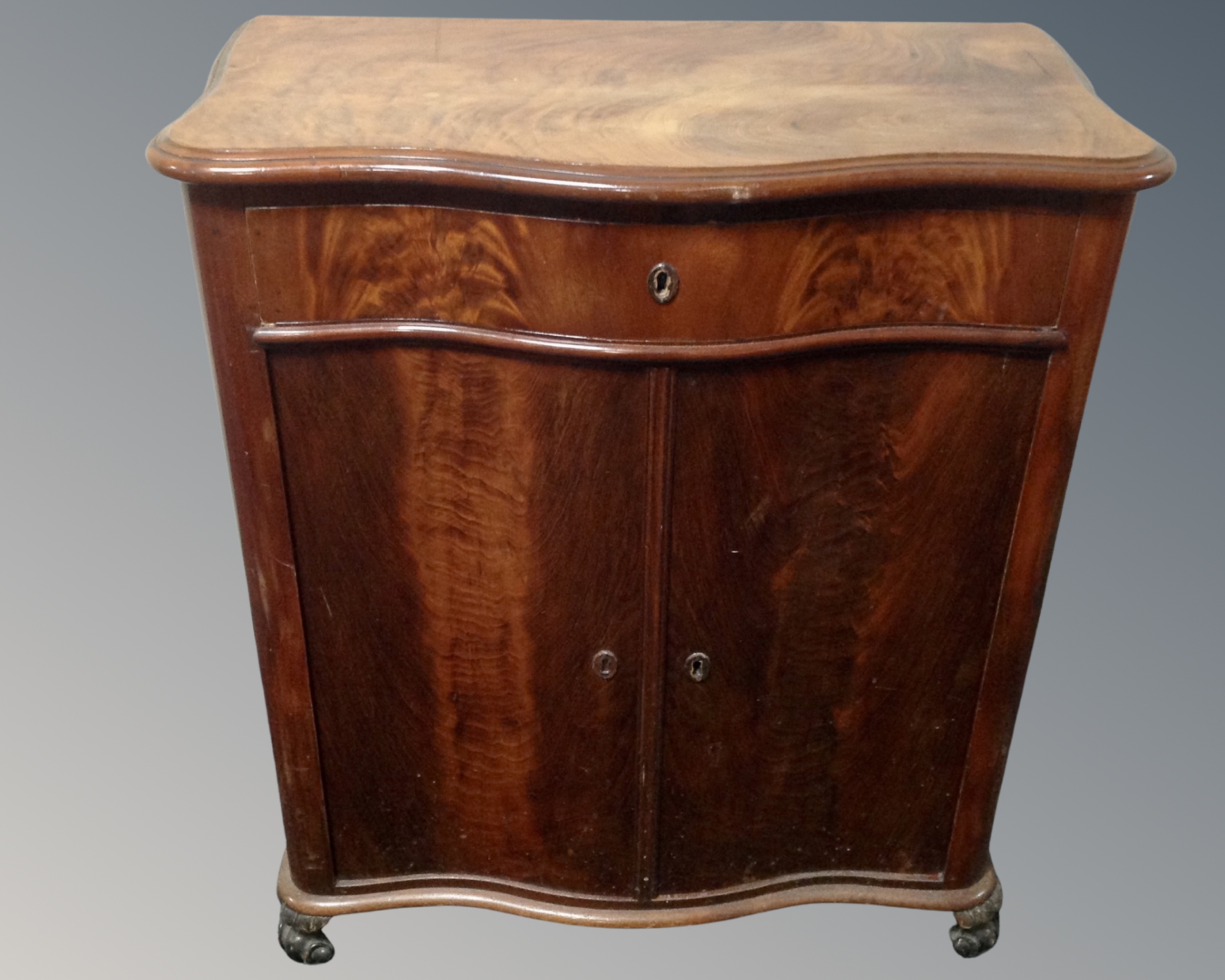 A 19th century mahogany serpentine fronted double door cabinet fitted with a drawer.