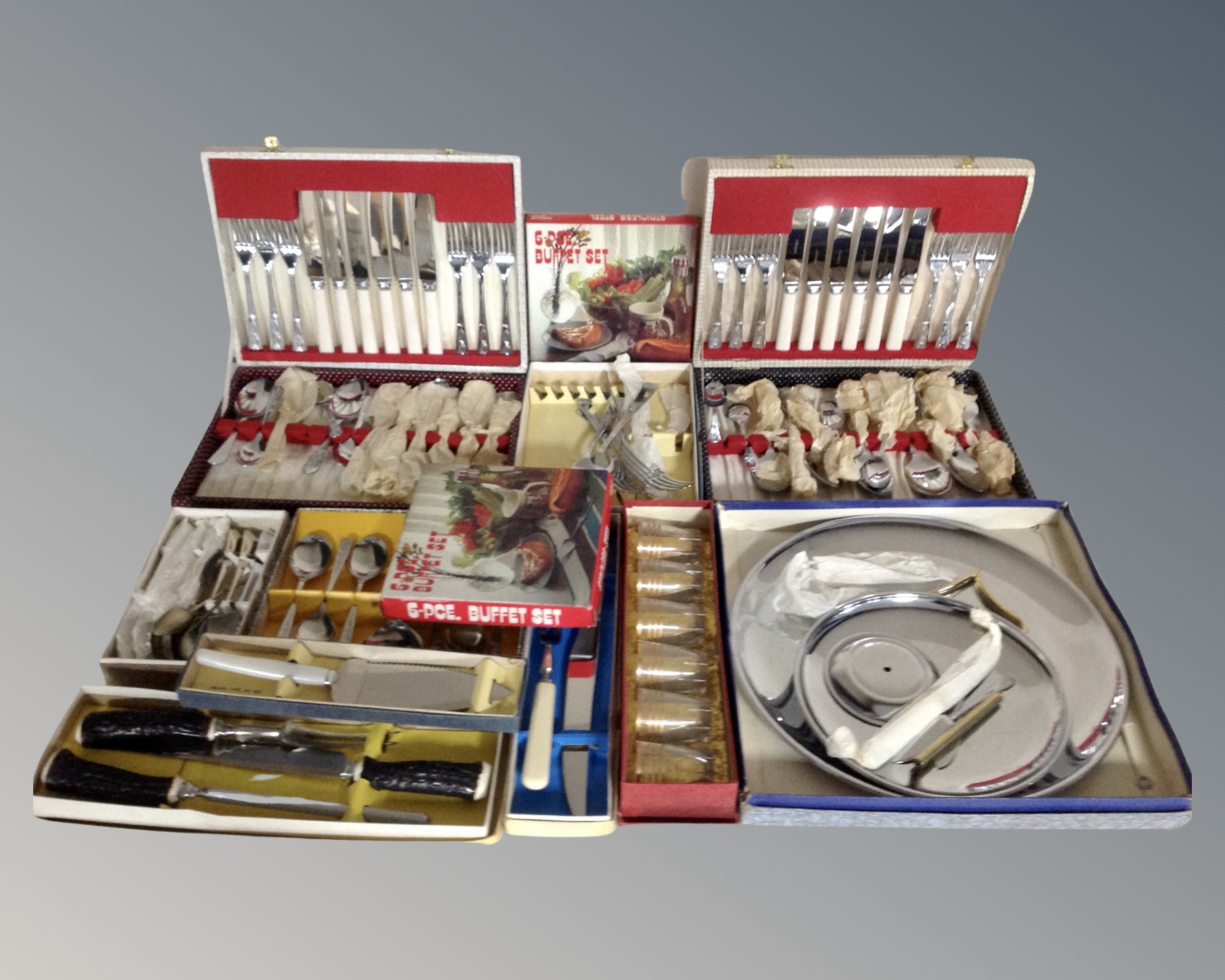 A vintage luggage case containing boxed cutlery including serving spoons, tea spoons, carving sets,