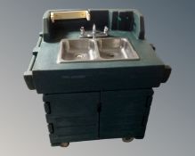 A stainless steel commercial double sink unit with taps inset into a vulcanized rubber cabinet.