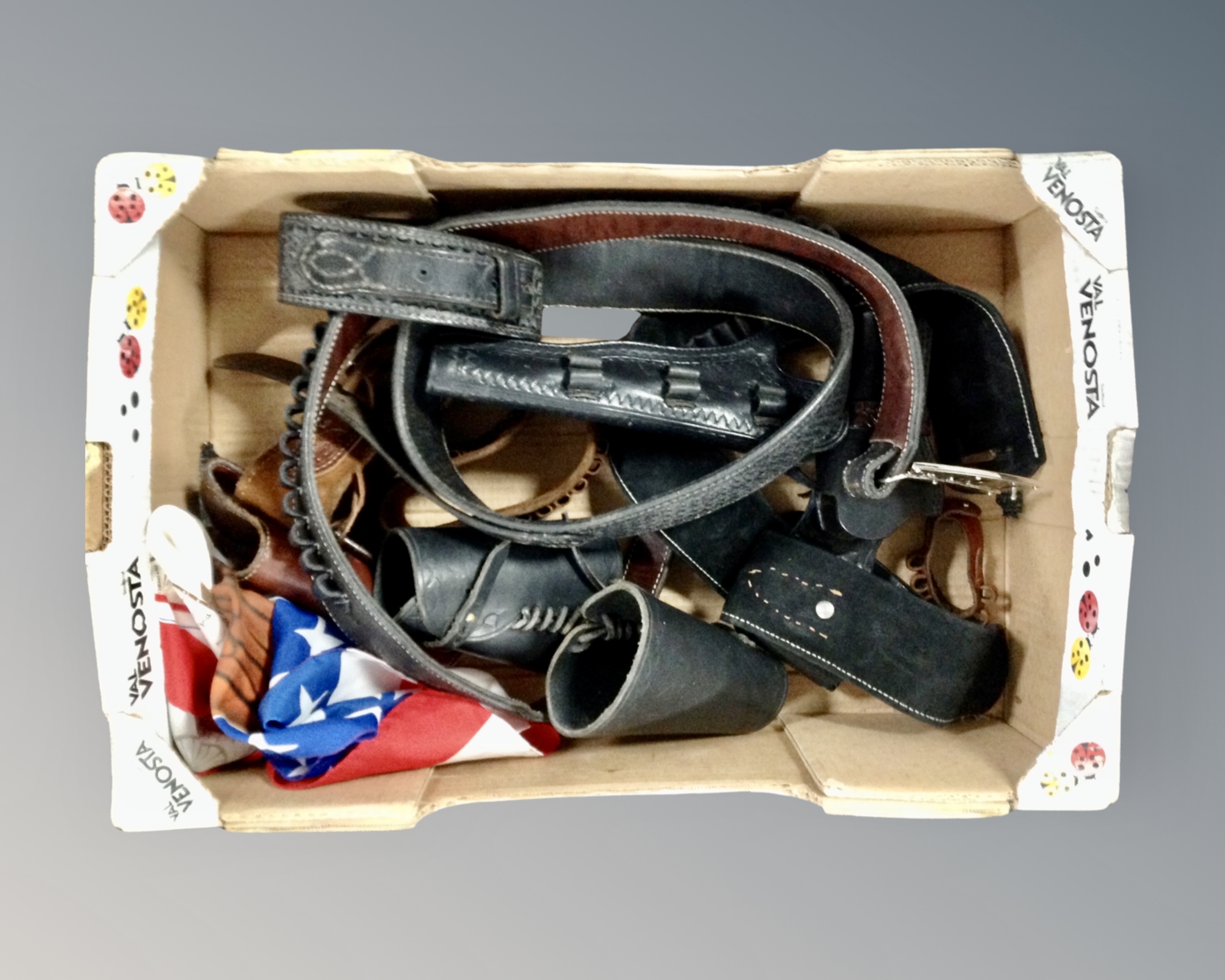 A box containing tooled leather gun belts, holsters and bandoliers together with a flag.