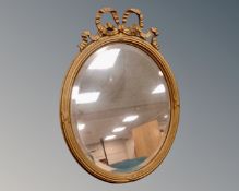 An oval bevel edged mirror in gilt frame surmounted by a bow.