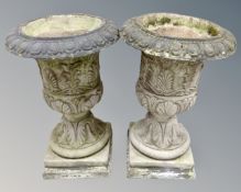 A pair of classical style weathered concrete garden urns on stands,