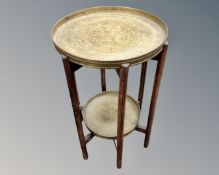 An Indian folding two tier occasional table with brass trays.