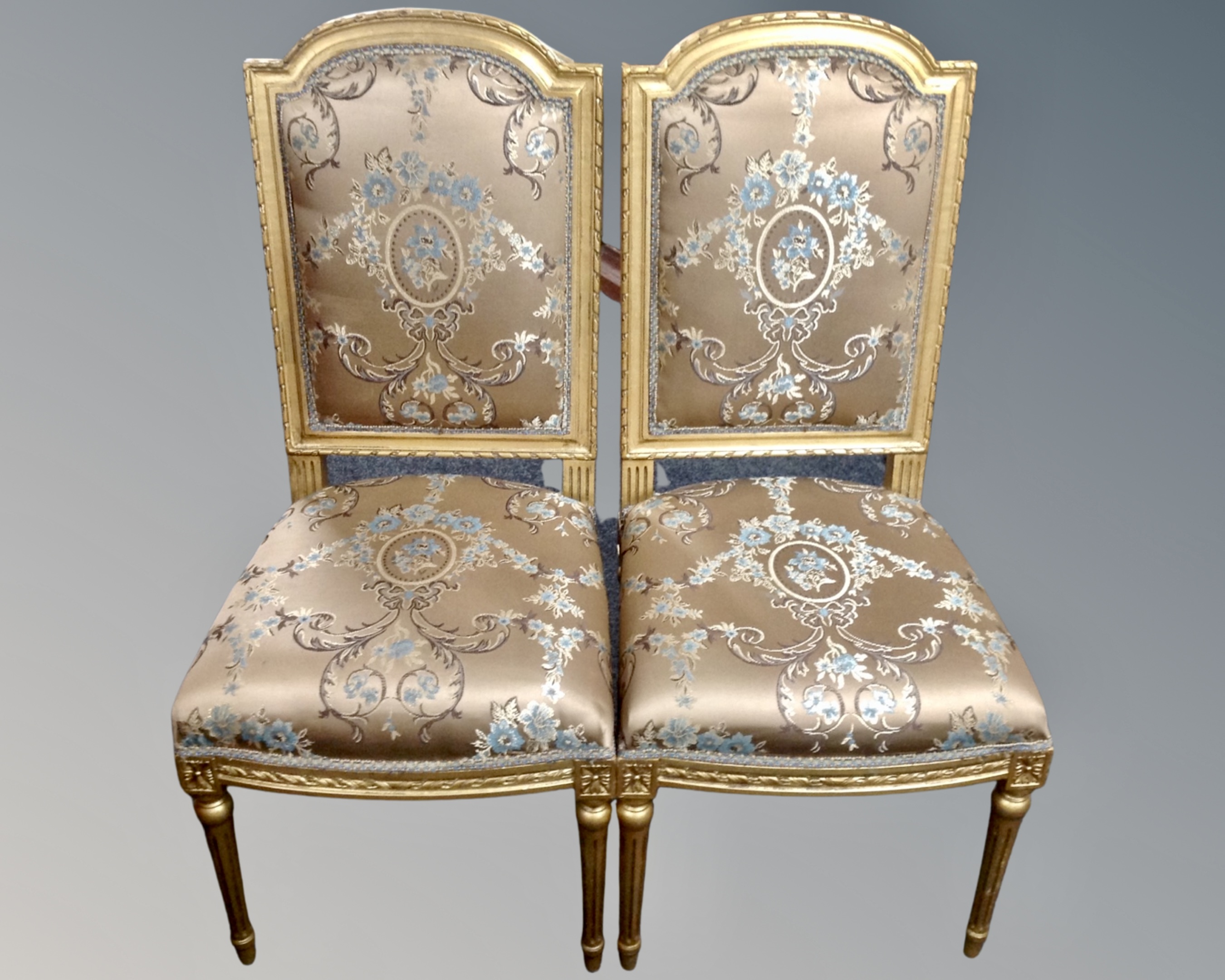 A pair of gilt dining chairs upholstered in a classical fabric.