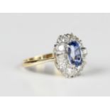 A gold and platinum, sapphire and diamond cluster ring, claw set with the oval cut sapphire within a