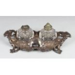 A Victorian silver rococo scroll moulded ink stand, the front with a pen rest beside two circular