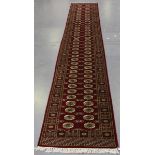 A Pakistan bokhara style runner, late 20th century, the claret field with two columns of guls,