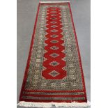 A Pakistan bokhara style runner, late 20th century, the red field with a single column of lozenge