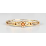 A gold, coral and seed pearl oval hinged bangle, circa 1910, the front in a flowerhead and foliate