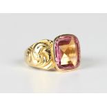 A gold ring, mounted with a curved rectangular pink tourmaline between scrolled shoulders,