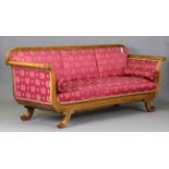 A Regency style satinwood framed settee, upholstered in patterned claret damask, raised on scroll