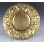 An early 20th century Arts and Crafts brass charger, the raised rim with repoussé work flowerheads