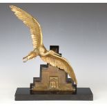 Edouard Guy - an Art Deco brown patinated and gilt bronze model of a stork flying above a temple