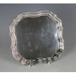 A George V silver shaped square card salver with raised scroll rim, on scroll legs, London 1914 by
