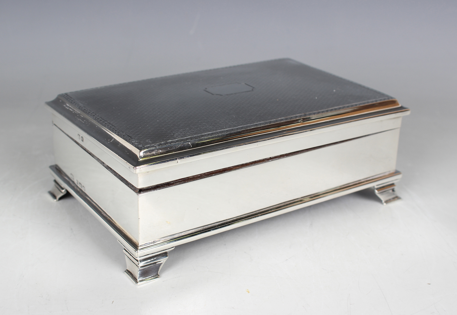 A George V silver rectangular trinket box with engine turned hinged lid, on bracket feet, with