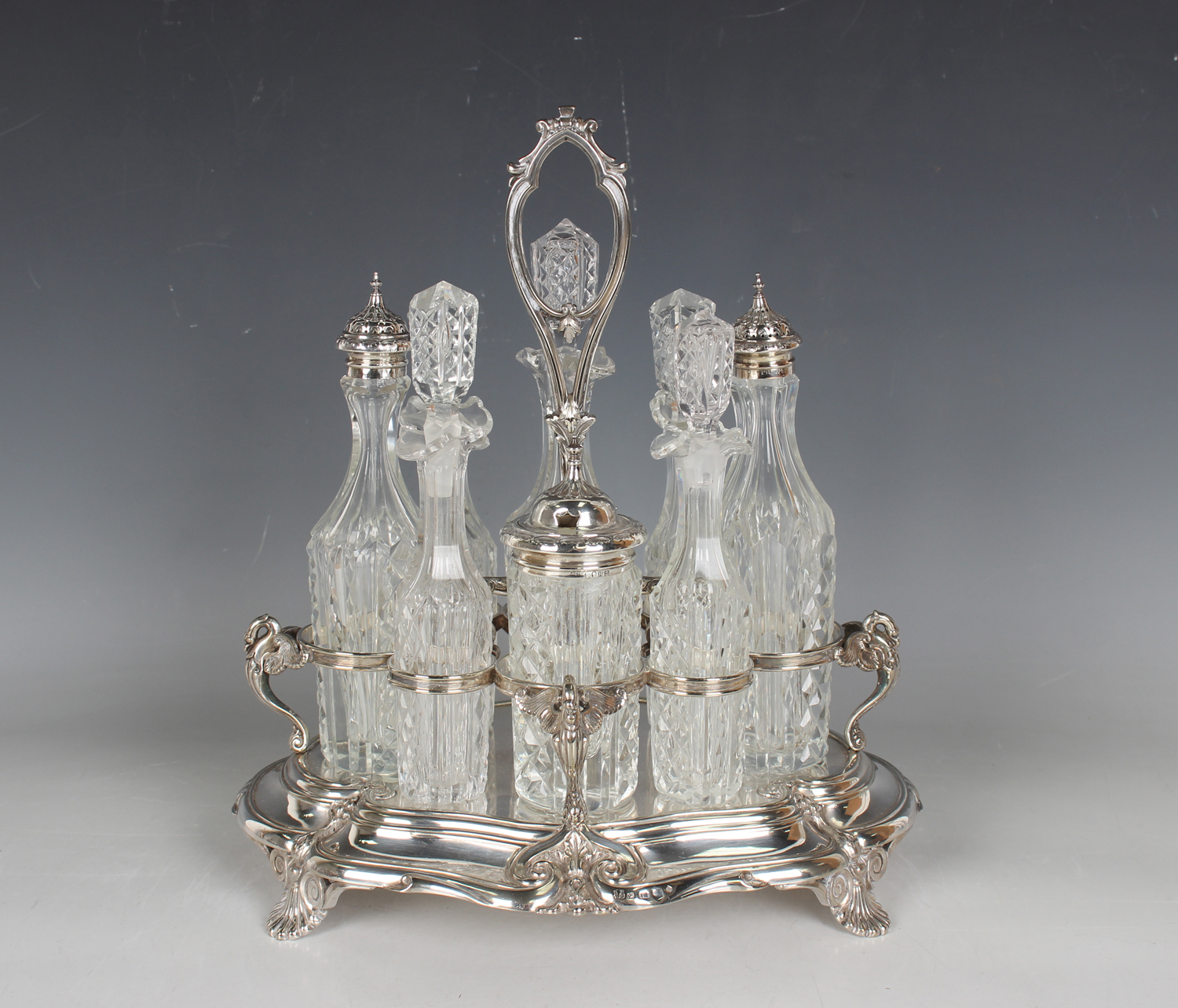 A late Victorian plated eight-bottle cruet stand with central scroll handle above swan supports,