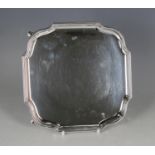 A George V silver square card salver with serpentine shaped corners, raised on scroll legs,